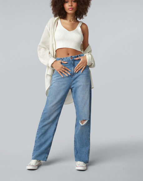 Uma mulher usando cropped de lã branco com um cardigã alongado creme, calça jeans clara e tênis all star branco 