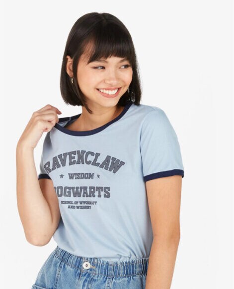 Uma menina vestindo uma camiseta azul da casa Ravenclaw de Harry Potter com expressão de felicidade. 