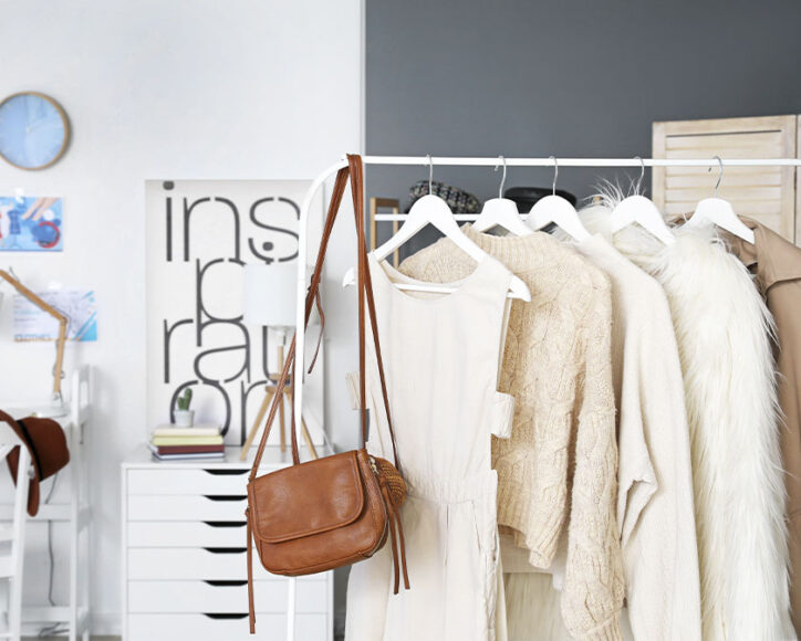 Uma arara de roupas com uma bolsa marrom, vestido regata creme e vários casacos peludos 