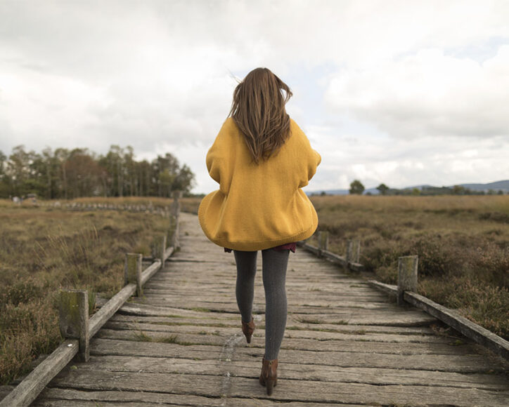Uma mulher vestindo uma meia calça grossa, salto marrom e um moletom grande amarelo
