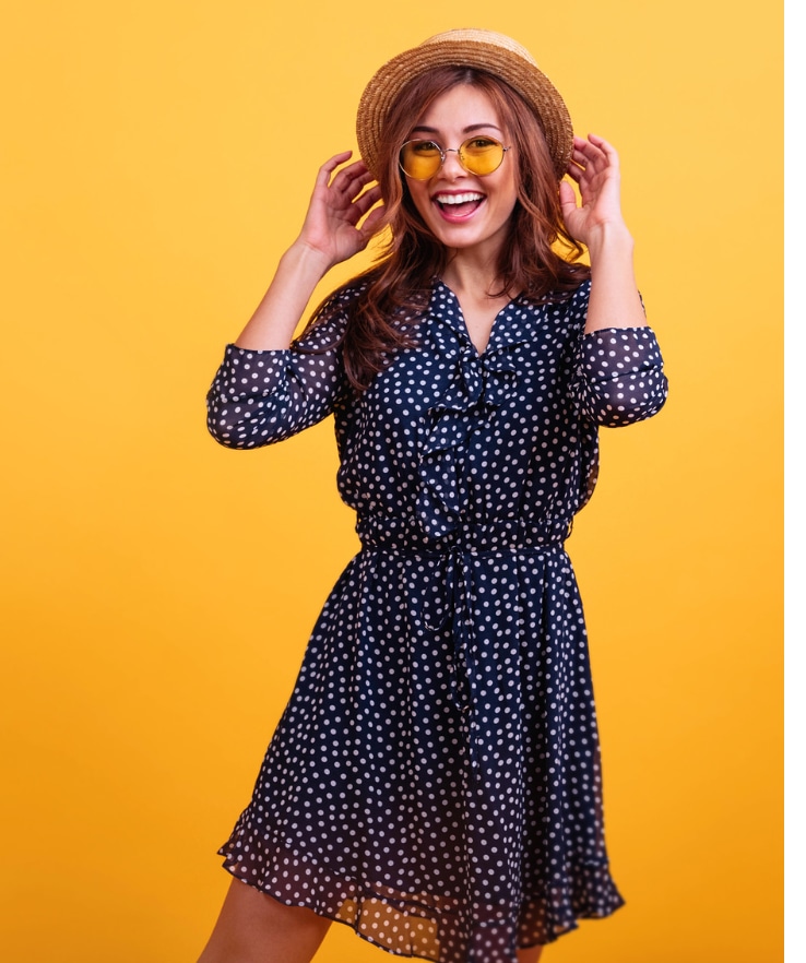 mulher sorridente fazendo pose para tirar uma foto com as duas mãos no chapéu